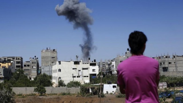 A Palestinian man stands looking at smoke rising from a building after an Israeli air strike in Gaza City, on July 9, 2014. (Photo: AFP-Thomas Coex)