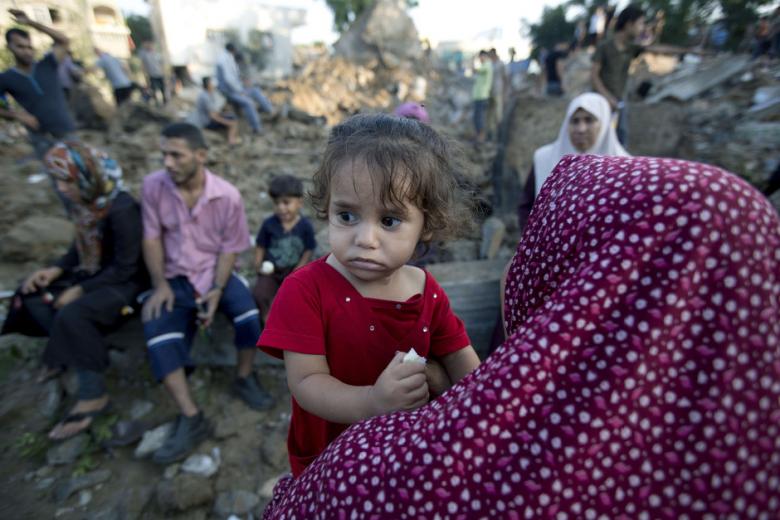 A Palestinian woman carries her daughter past rubble from a home which was destroyed in an Israeli air strike in Beit Hanoun, in the northern Gaza Strip, on July 9, 2014. (Photo: AFP - Mohammed Abed).